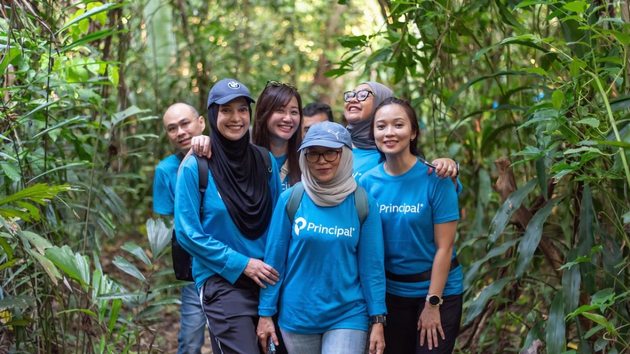 Group of people wearing blue Principal Financial Group shirts in a forest.