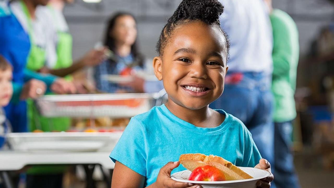 A young child smiling while holding a bowl of food