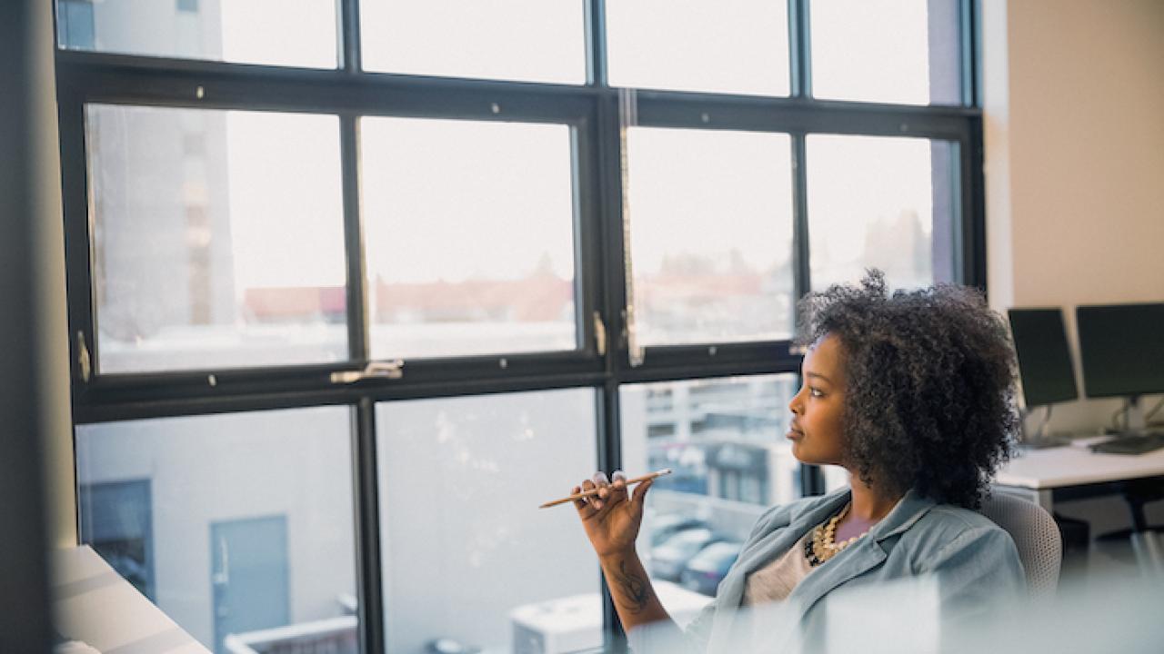 Woman sitting at her desk at work and looking out of a window.