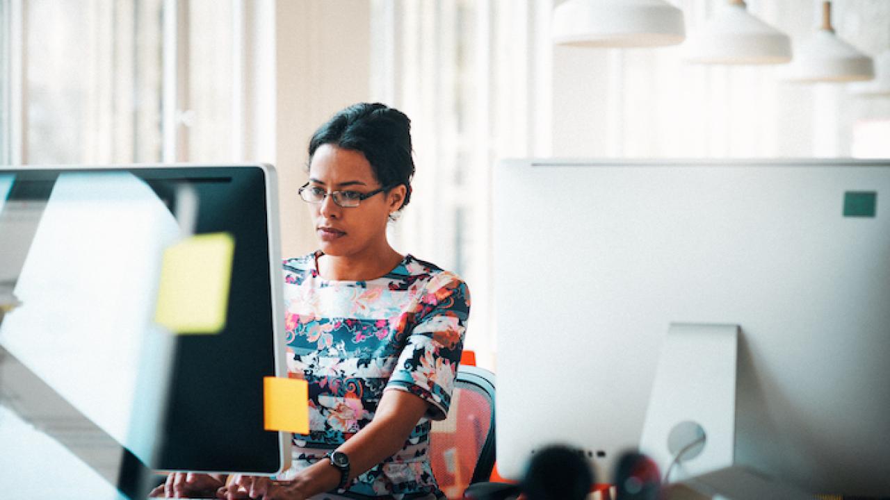 Woman seated at her desk behind a computer monitor.