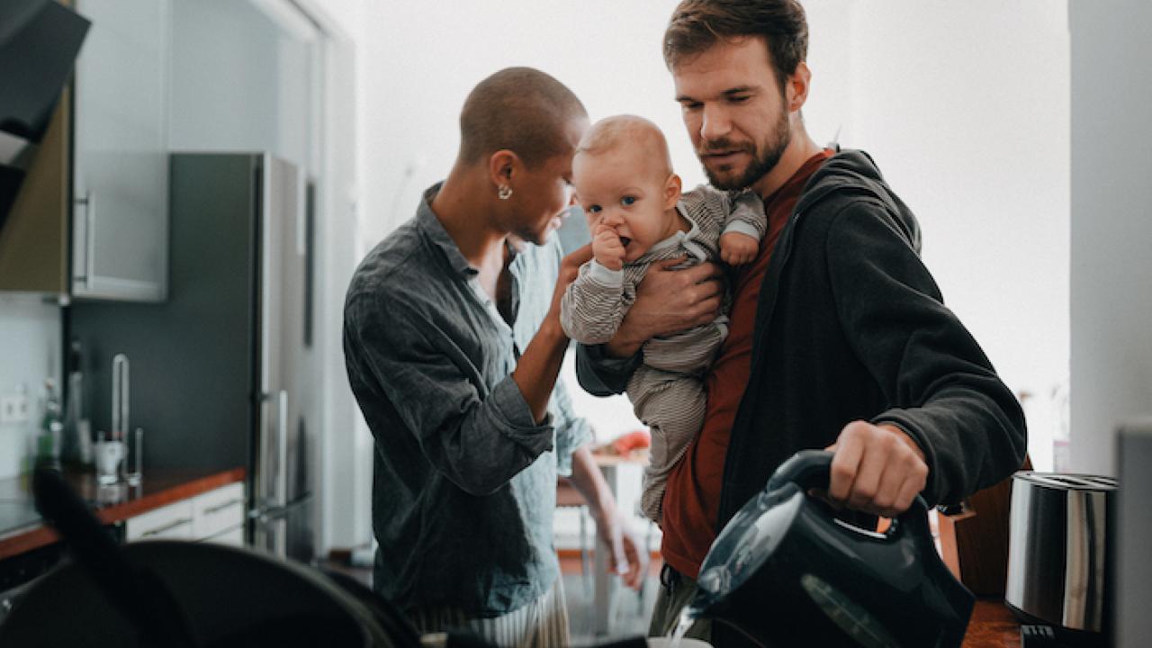 Two male parents getting ready for work in the morning and holding their son.