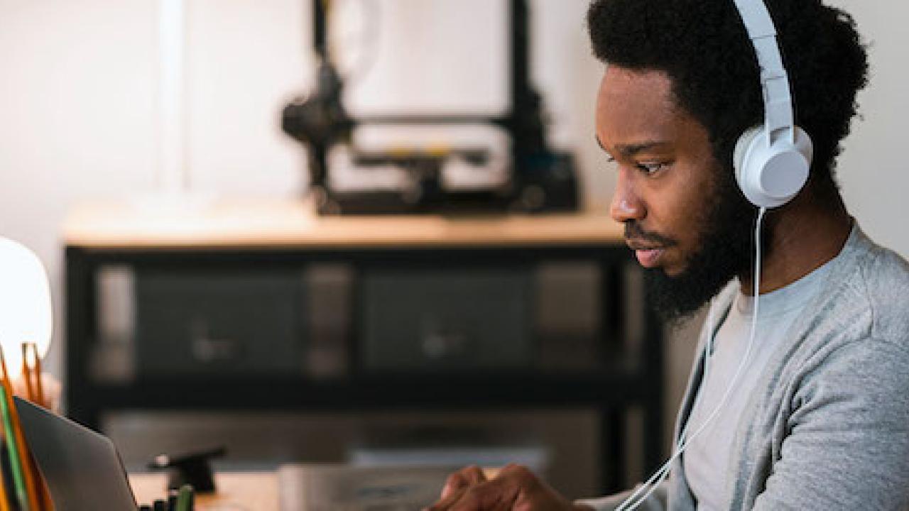 Black male wearing headphones is seated in front of a computer.