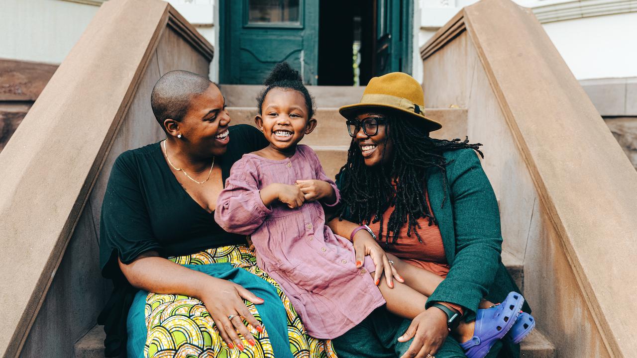 Two smiling Black women sitting on front stoop with a young, smiling Black girl