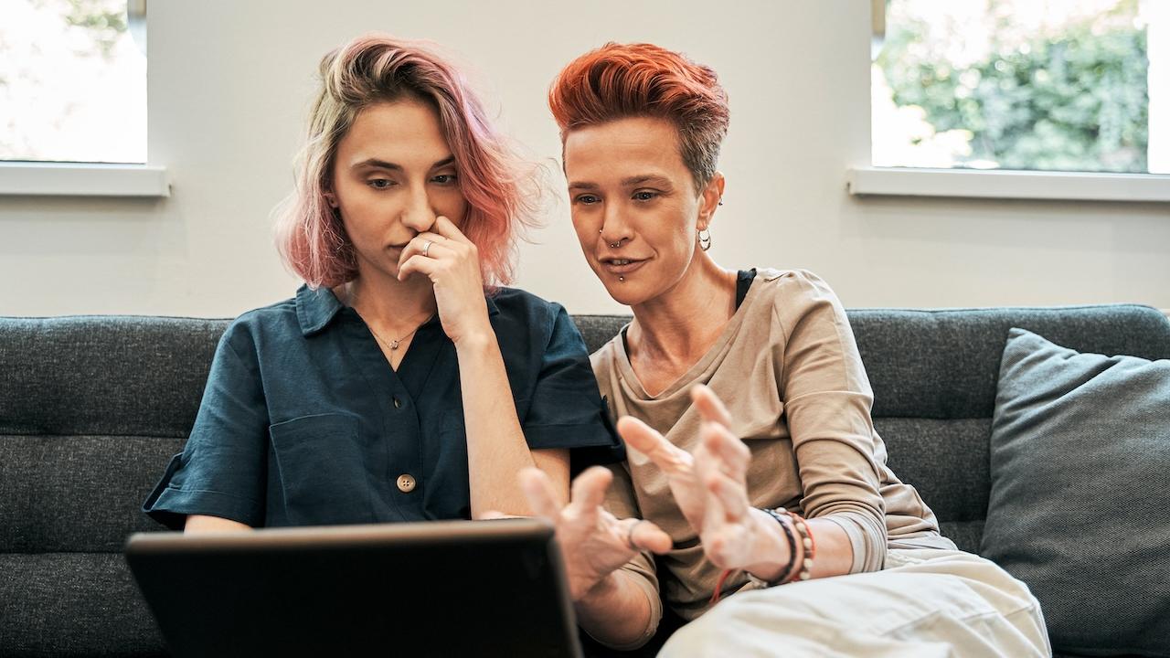 Two people seated on a couch looking at a laptop.