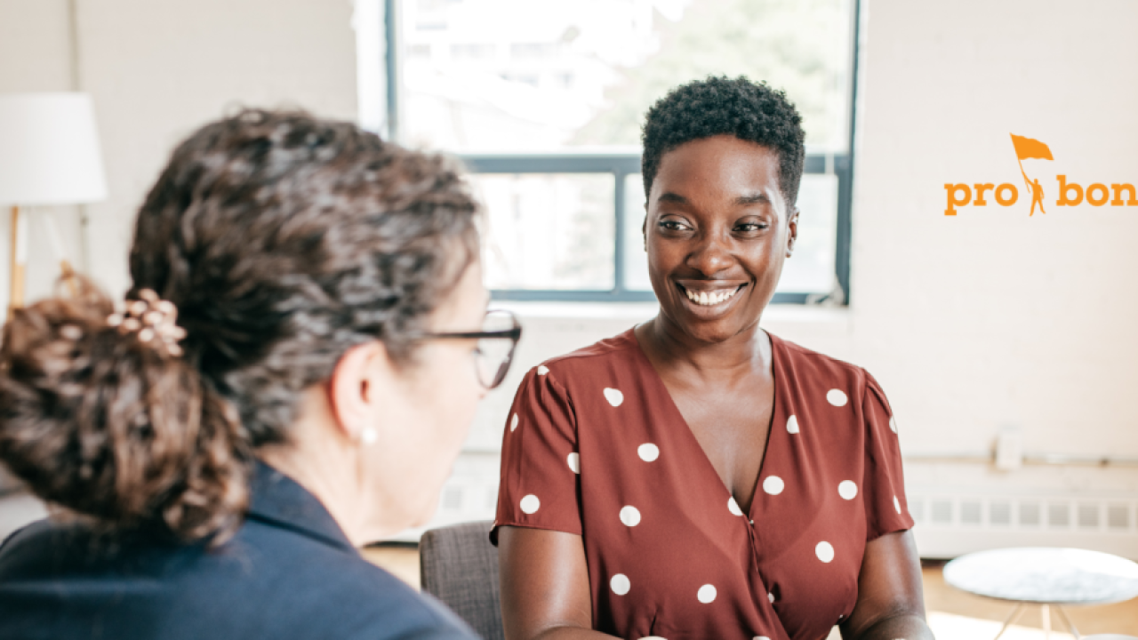 two smiling women talk at a table in a white room