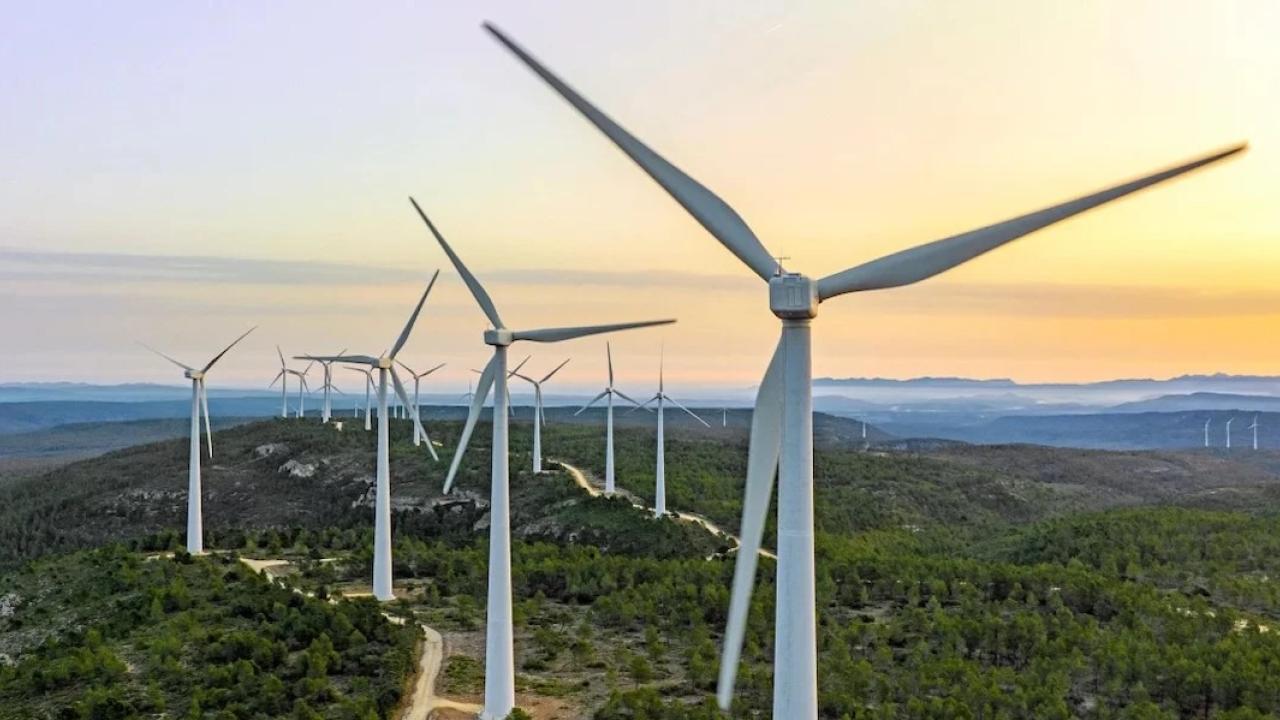 Windmills on top of a hill with the sun setting in the background.