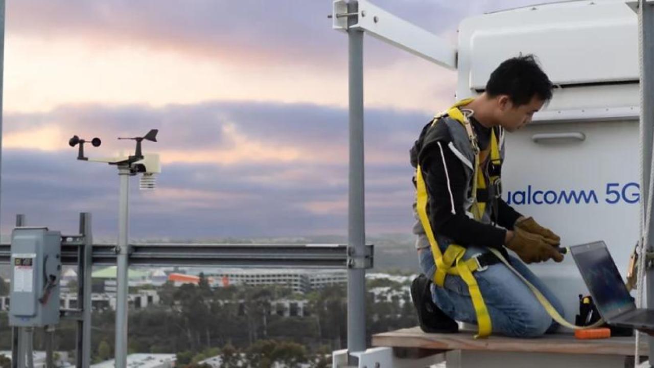 People working on top of a building in front of a Qualcomm 5G device