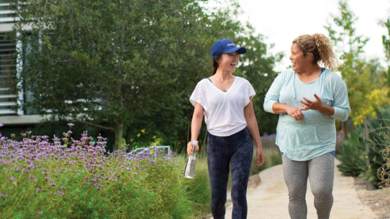 Two people walking on a path together, talking. Lush plants to the sides.