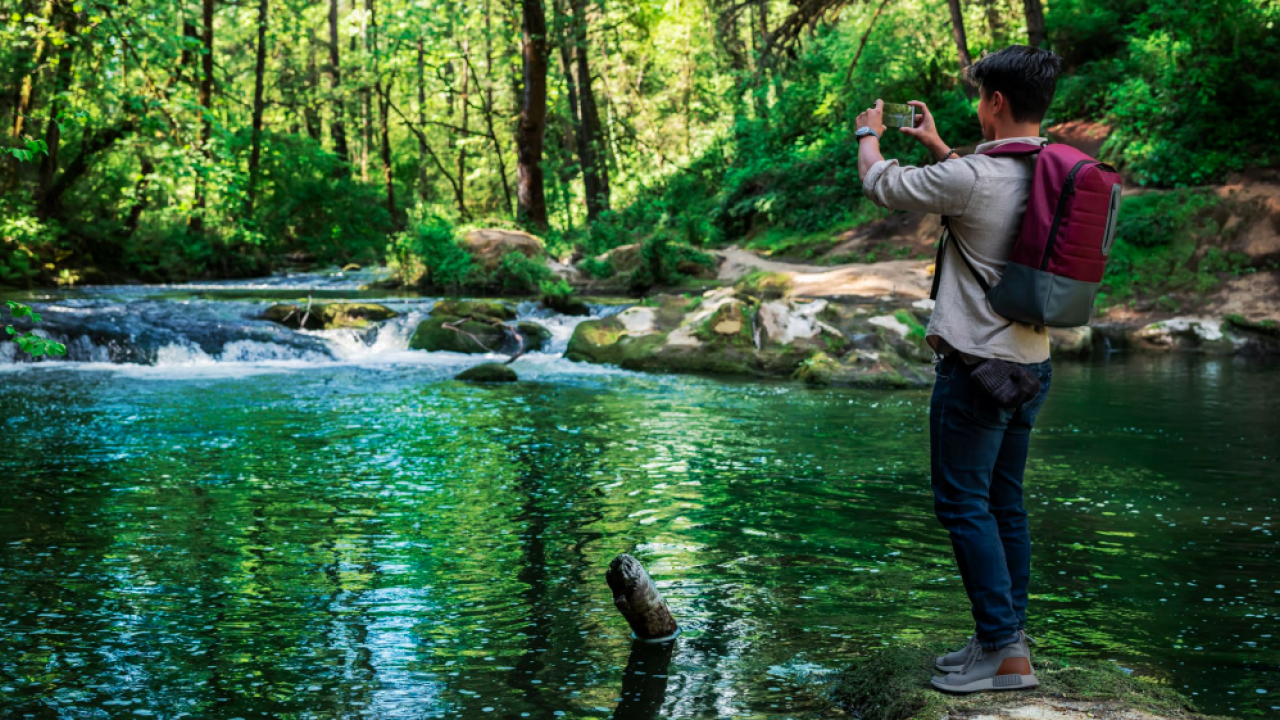 Person standing on a riverbank taking a picture of the water