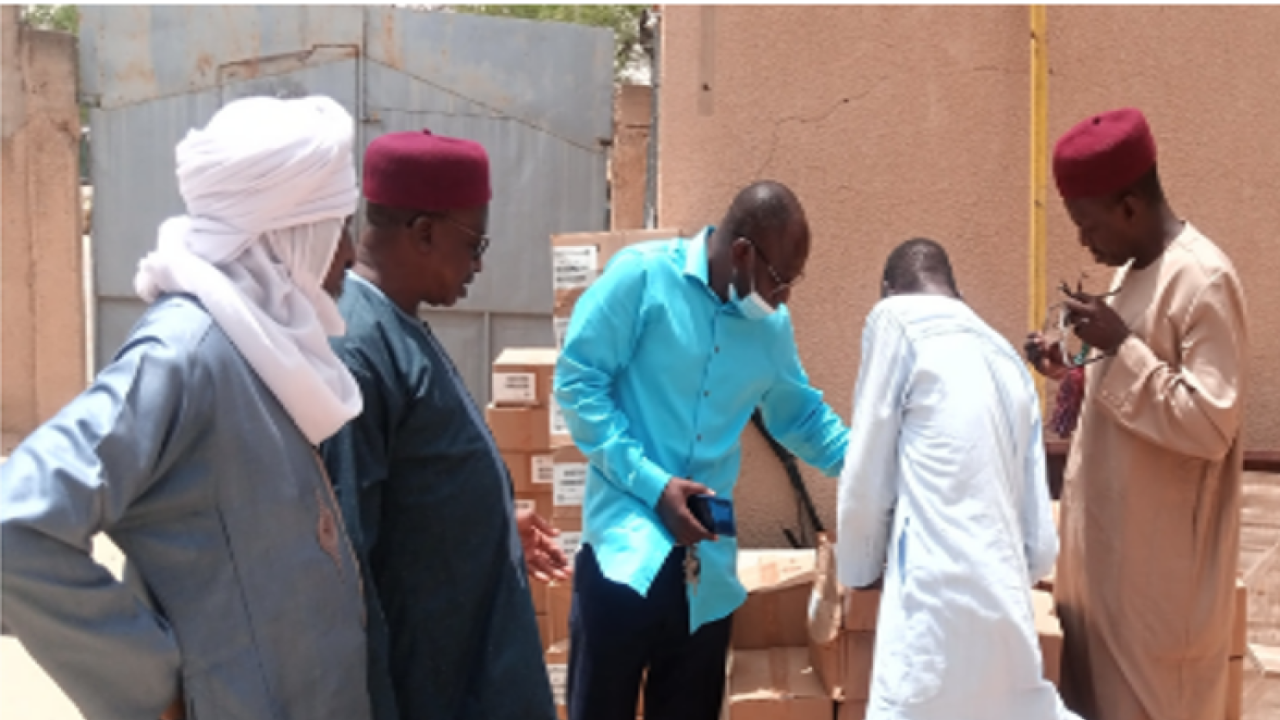 Five people look over a stack of boxes outside a gated concrete wall.