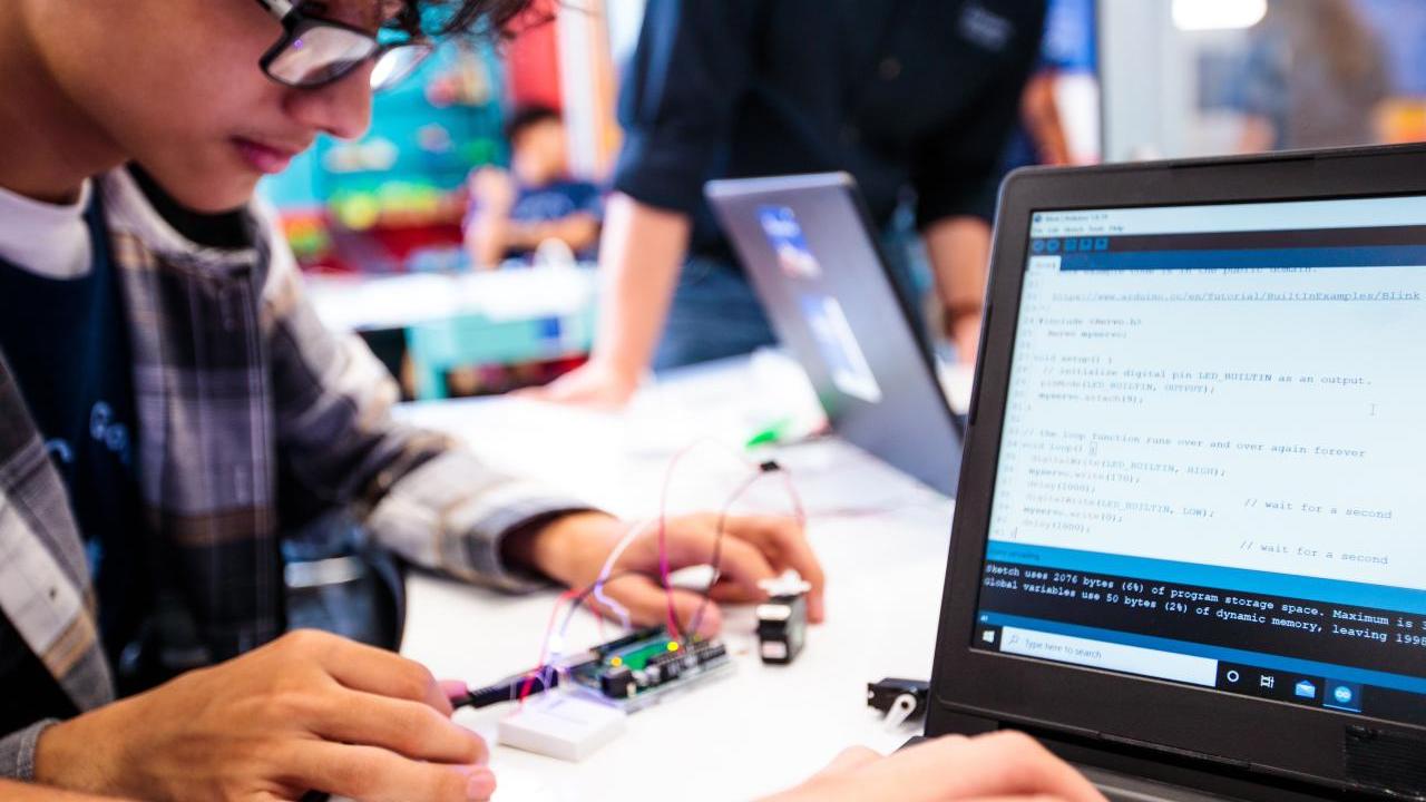 students work on a small circuit board and a laptop