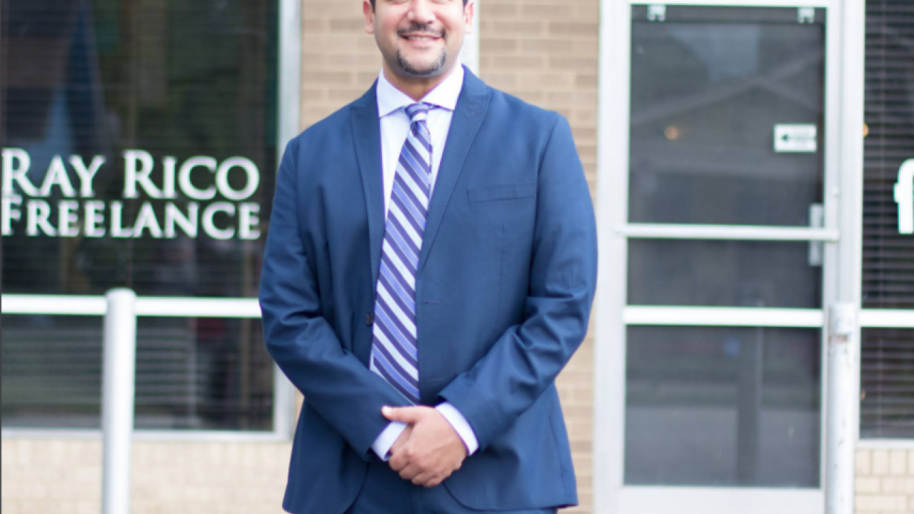 Ray Rico standing outside their business. Wearing a blue suit and striped tie.