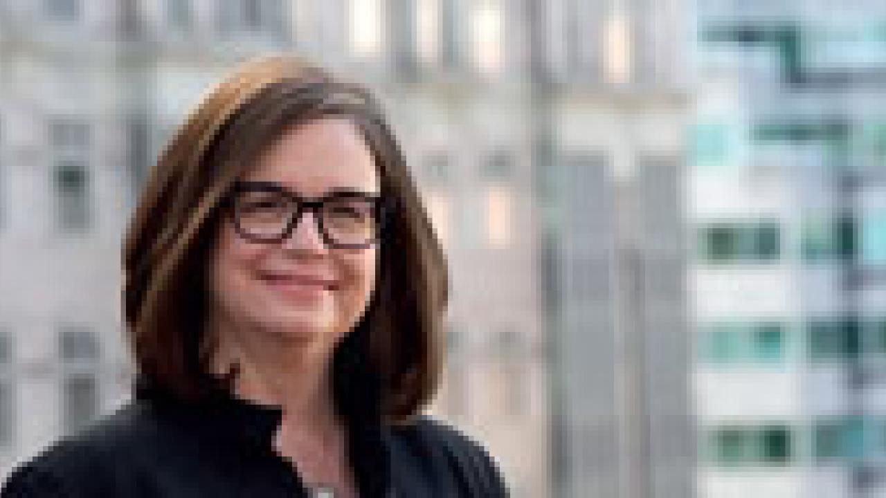 Headshot of a woman with shoulder-length brown hair and black-rimmed glasses