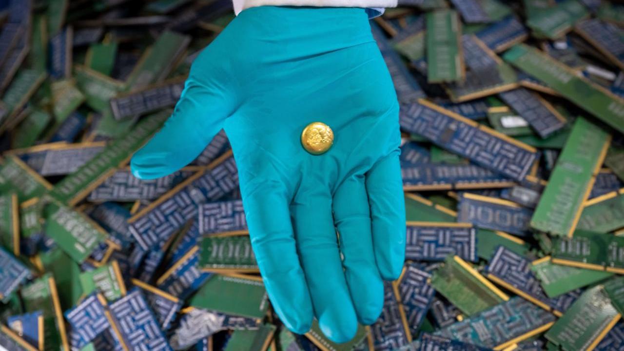 A person wearing gloves with a piece of recovered e-waste gold in the palm of their hand 