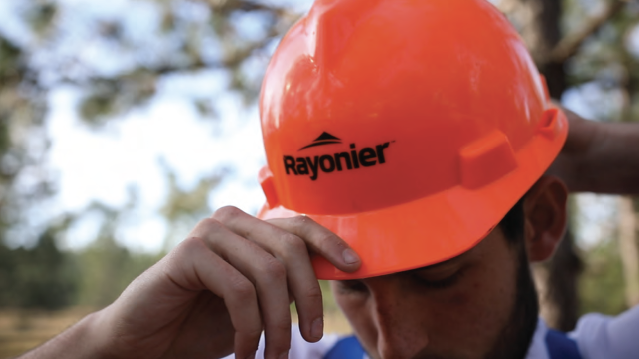 A person putting on a red safety hat with the Rayonier logo on the front