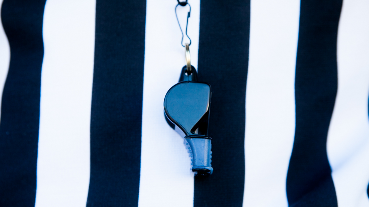 close up of black and white stripped referee shirt with blue whistle