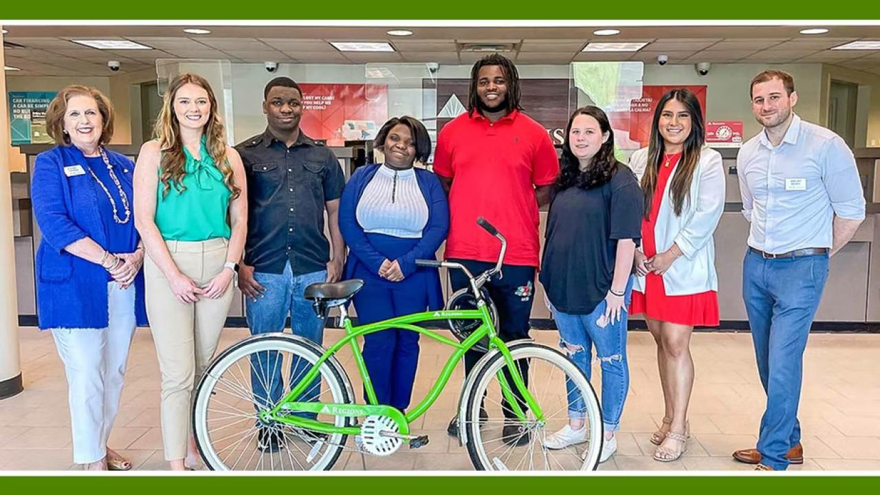 a group of eight people standing in a bank lobby, a green bicycle in front of them