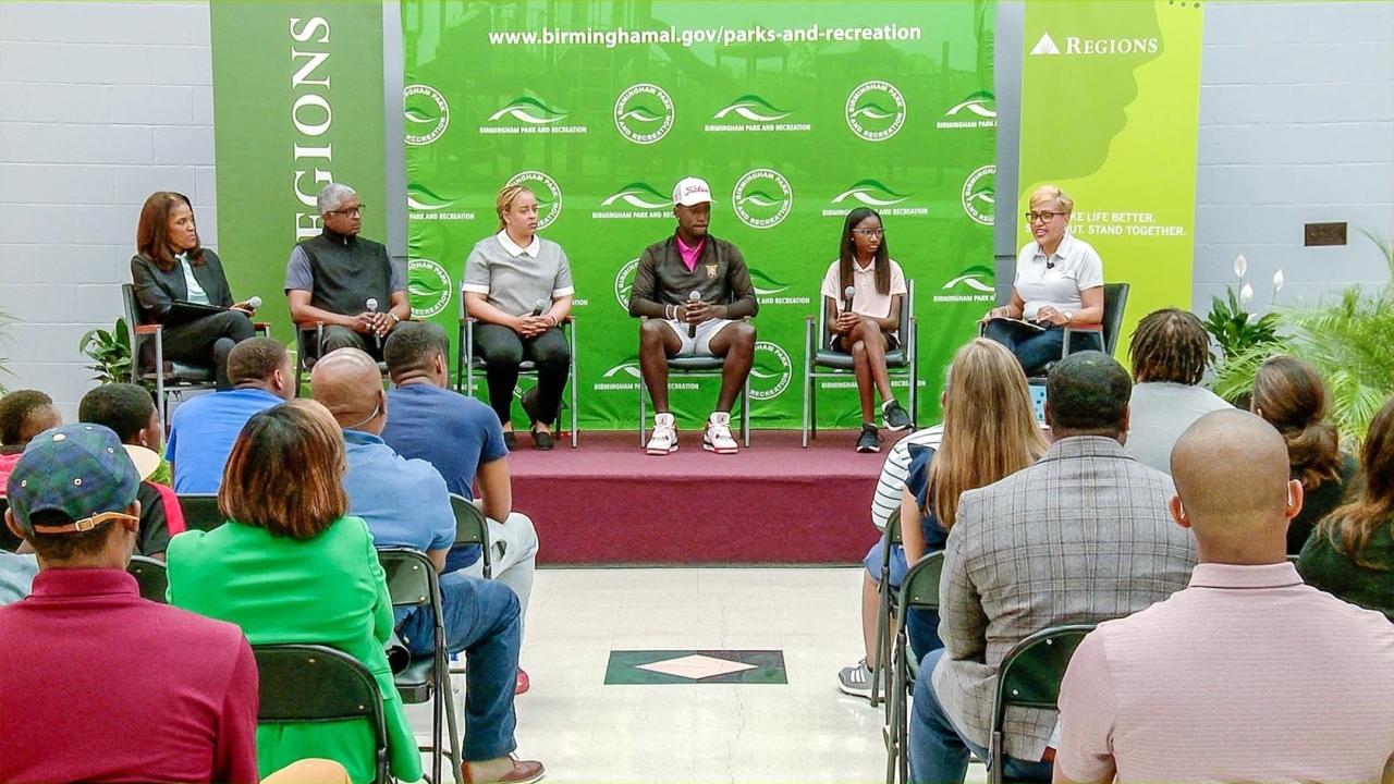 A panel of Black leaders, athletes, and students on a raised platform in front of a green backdrop