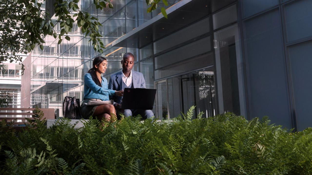 Two people sitting outside an office building looking at a laptop
