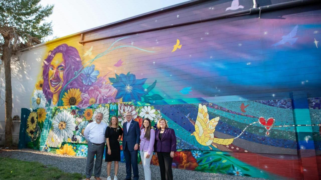 Group of people stood in front of a brick wall which has art on 
