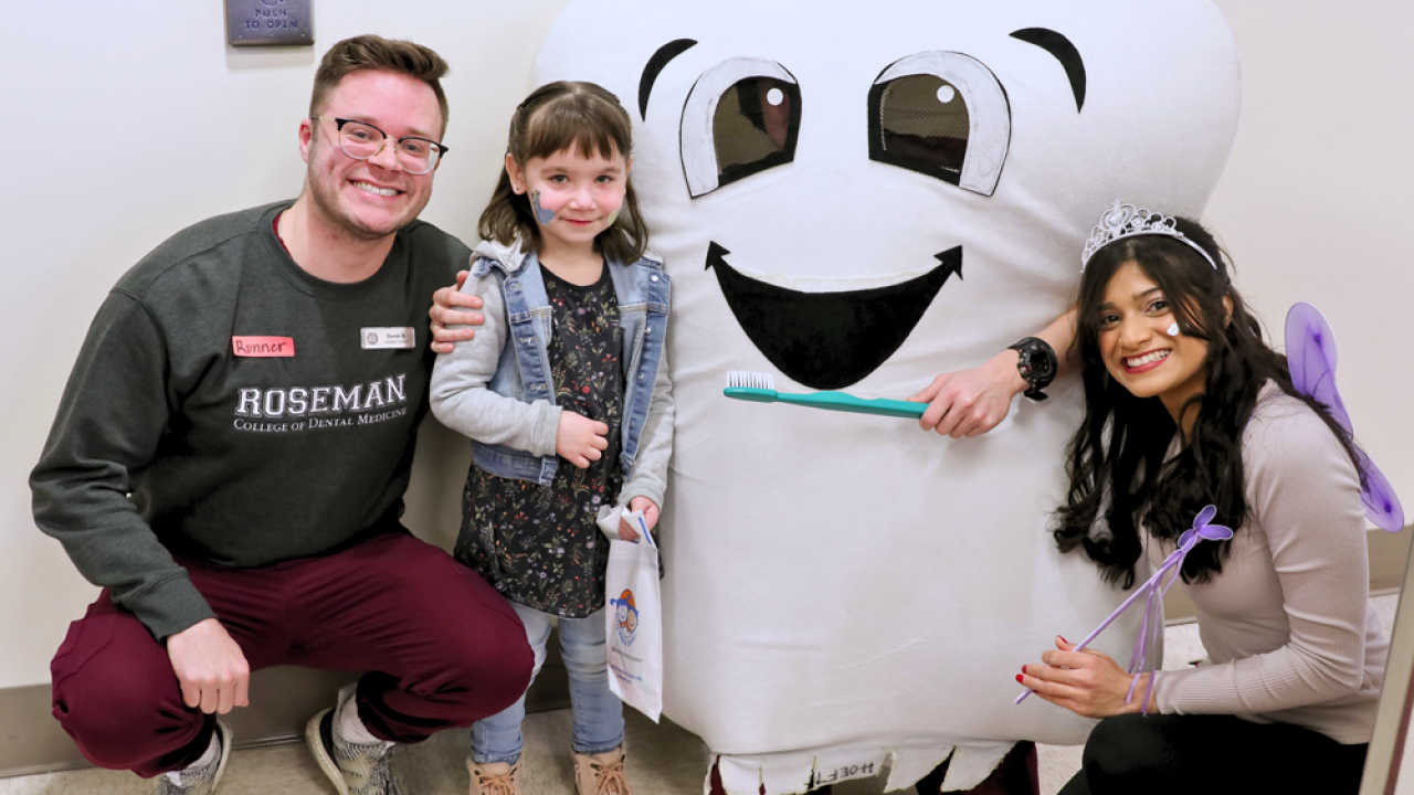 Two adults and a child next to a tooth mascot