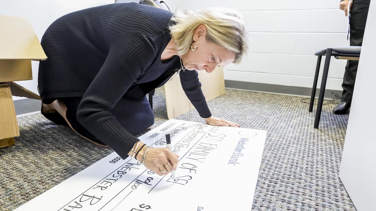 Grant check for $100,00.00 being made out by a representative from Webster Bank.