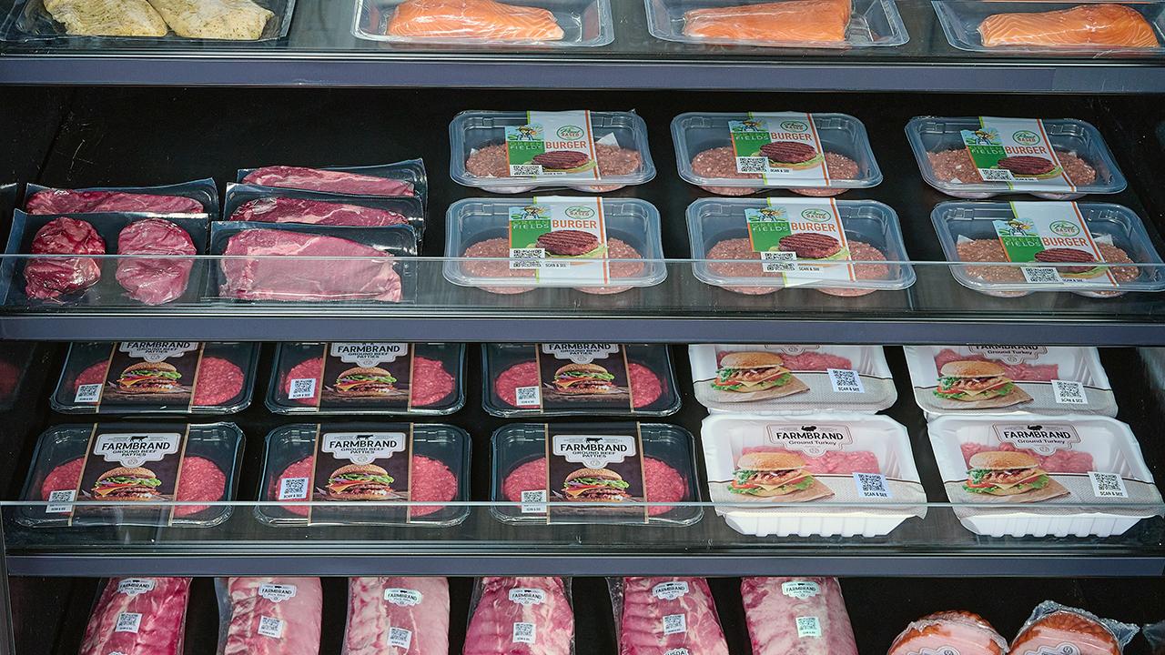 Packages of various proteins including meat and fish sitting on shelves in a refrigerated grocery store case