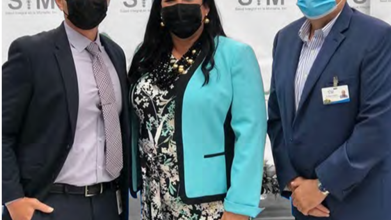 Three people wearing protective masks in front of a wall with SIM logos