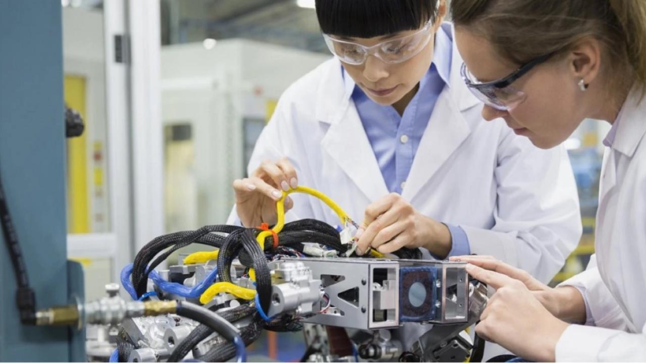two people wearing lab coats and safety glasses working on a piece of equipment