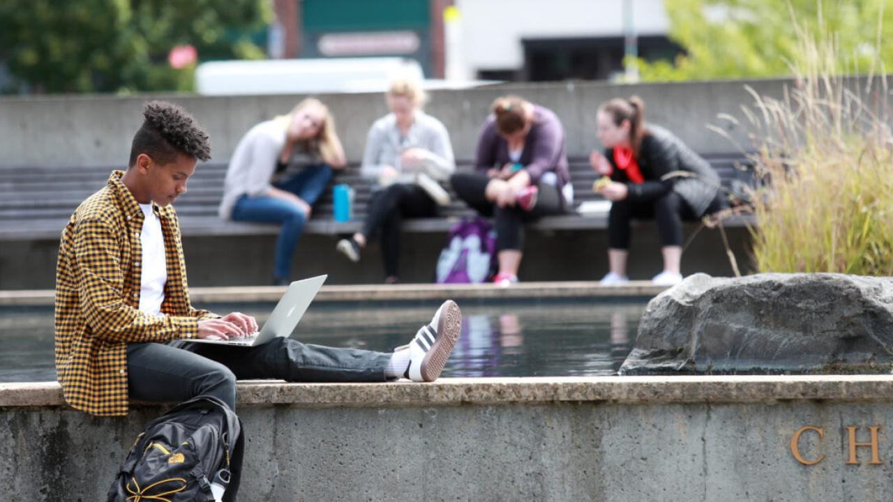 Student sat on a wall using their laptop 