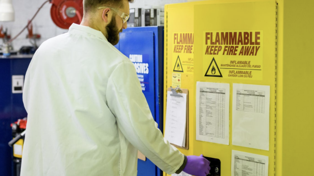 A person opening a yellow locker that has a fire hazard sign on the front of the door 