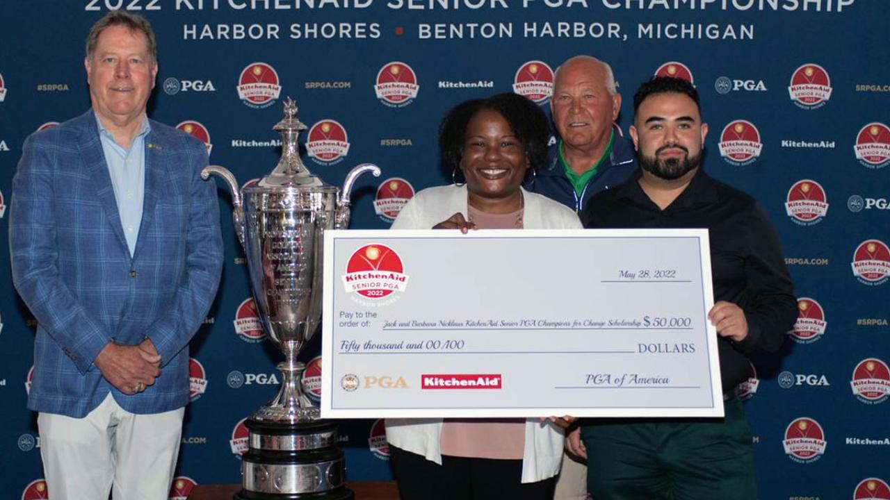 Both scholarship winners stand with a large check next to the PGA trophy and two presenters