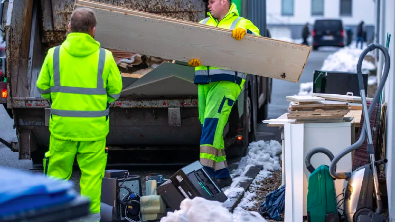 Men throwing old furniture boards into a garbage truck.