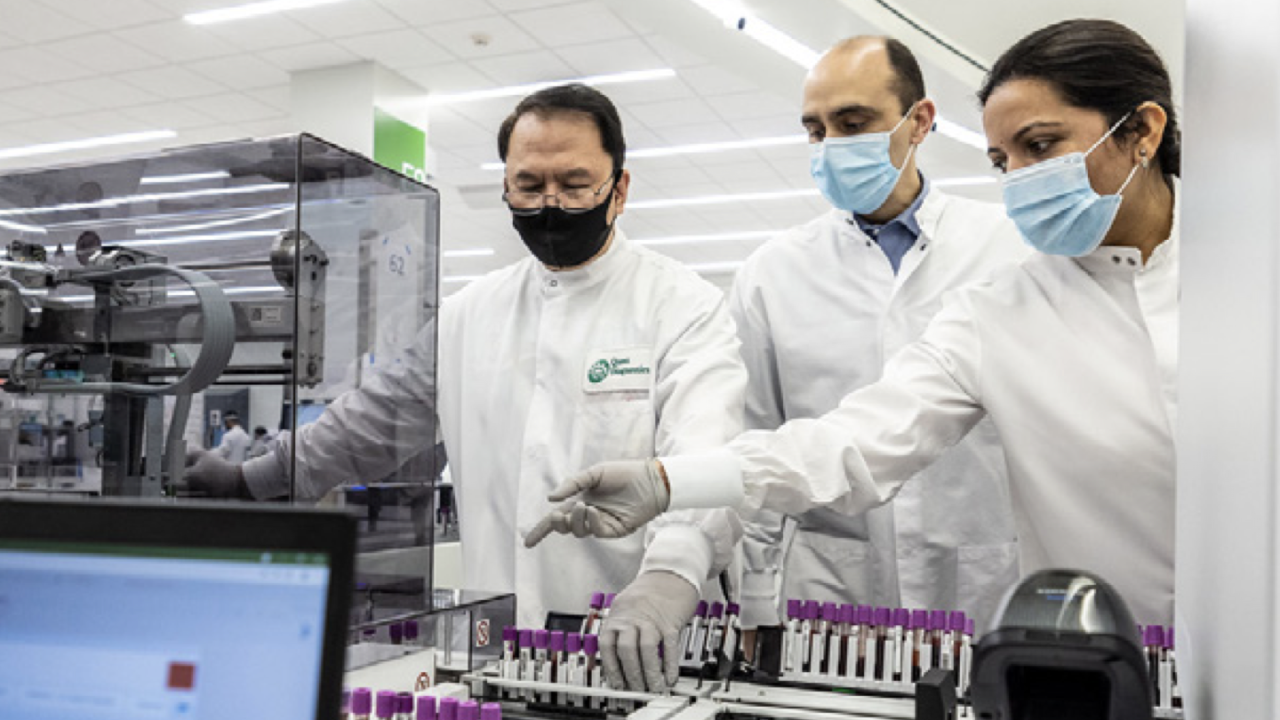 workers in white lab coats and face masks looking over test tubes