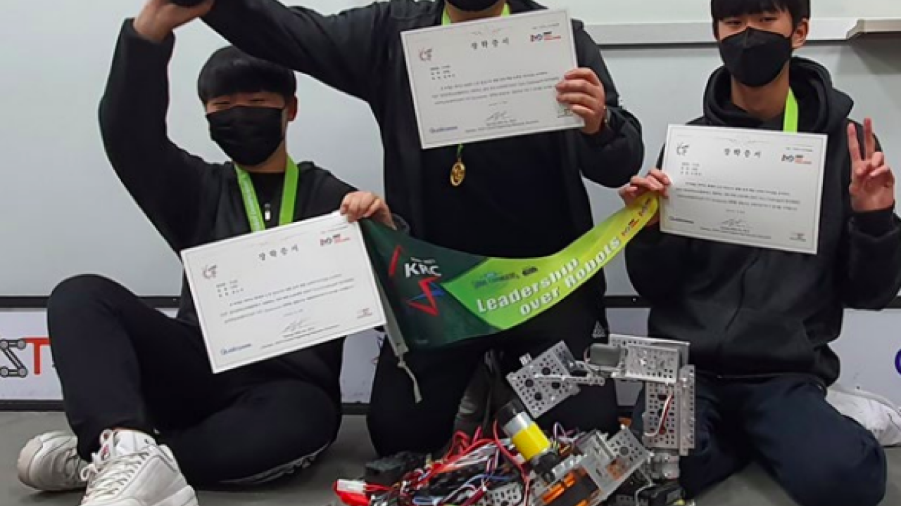 3 students kneeling behind a robot