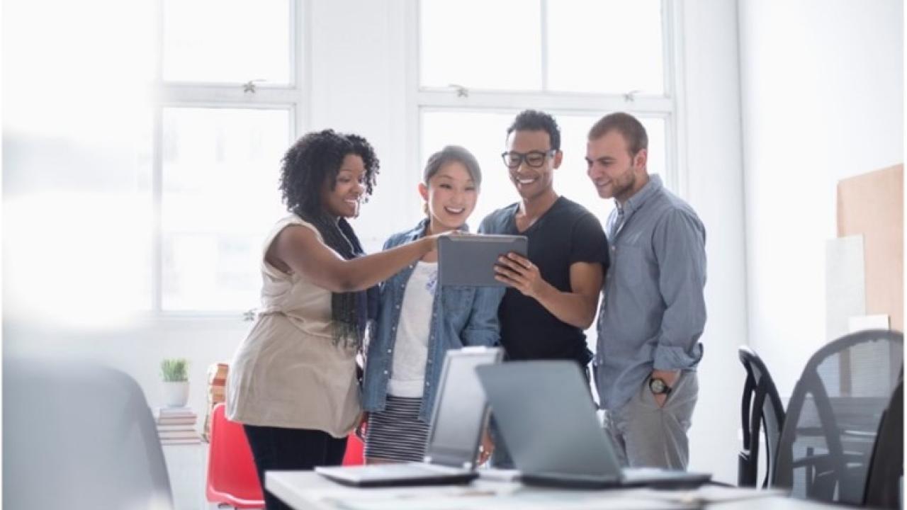 Two men and two women are sharing a tablet in a meeting room. 