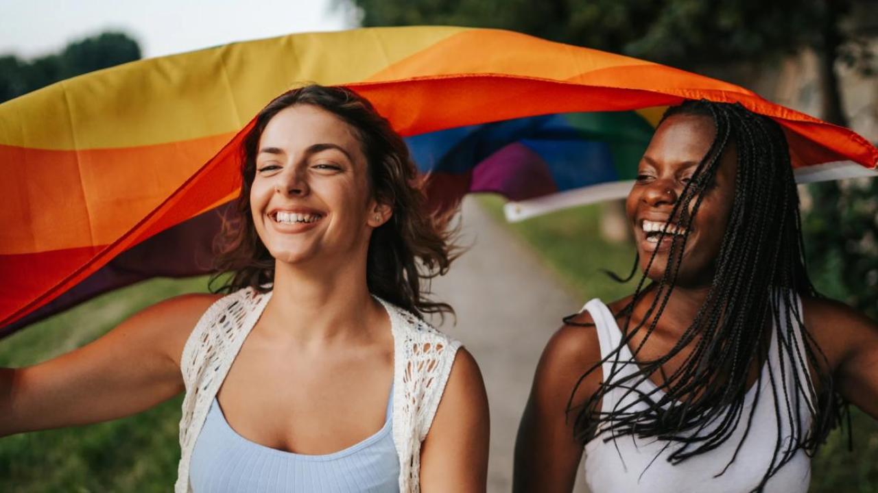 Two people smiling holding up the LGBTQ+ flag