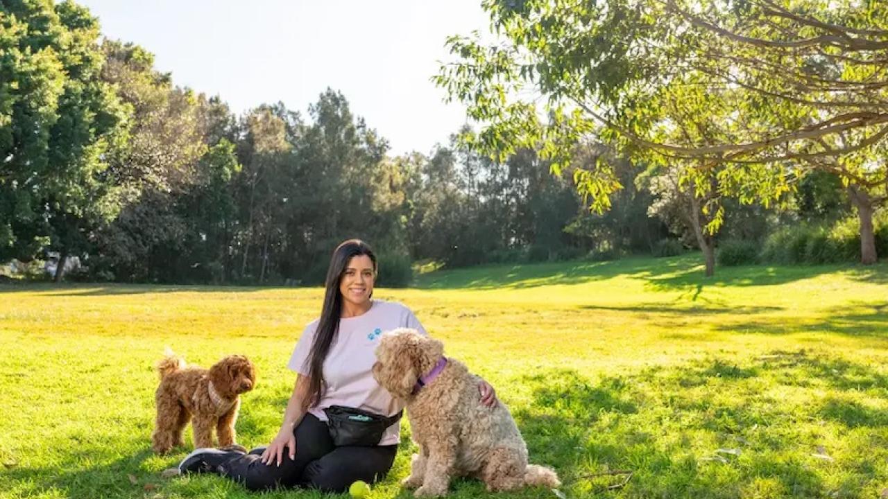 Young woman seated on the grass with her two dogs.