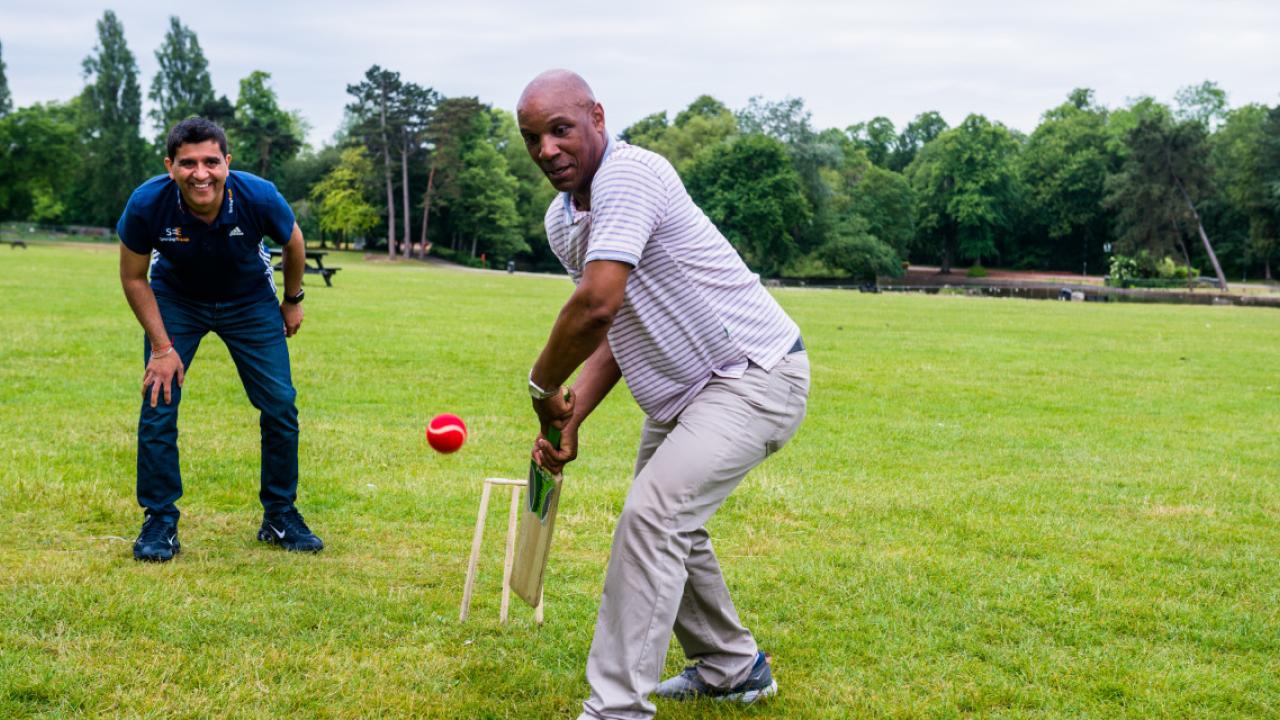 A black man playing cricket on a grassy field
