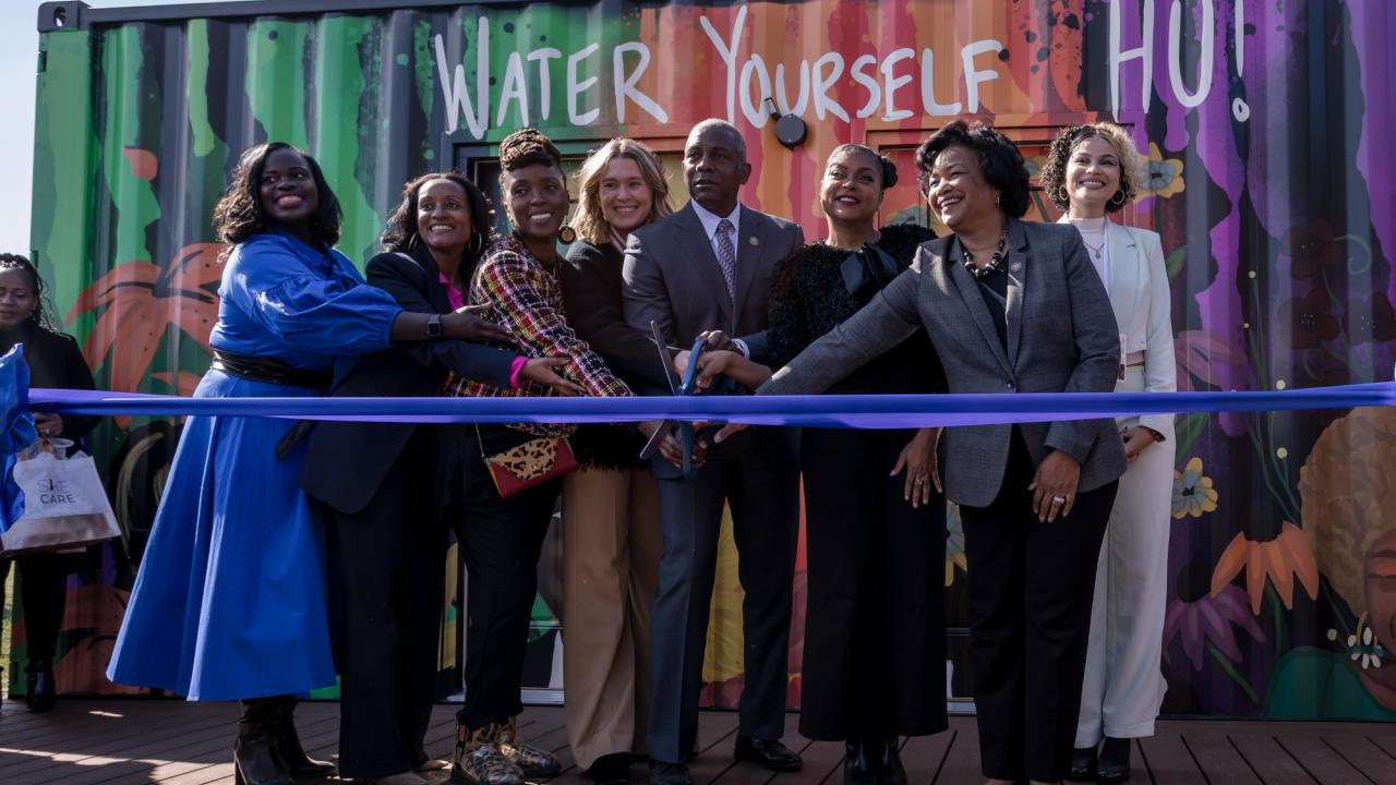 8 people cutting ribbon of a SheCare pod at Hampton University