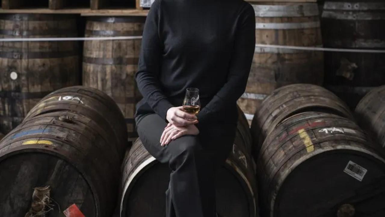 Stephanie MacLeod seated on a barrel, many barrels behind her.