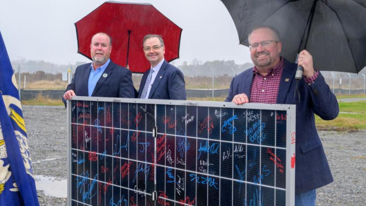 Three men holding umbrellas at opening of facility