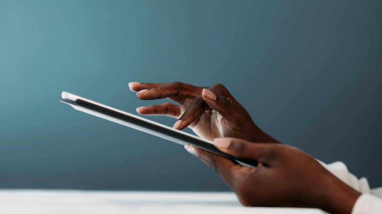 Close-up of a person’s hands using a digital tablet, with fingers gently tapping the screen against a soft blue background.