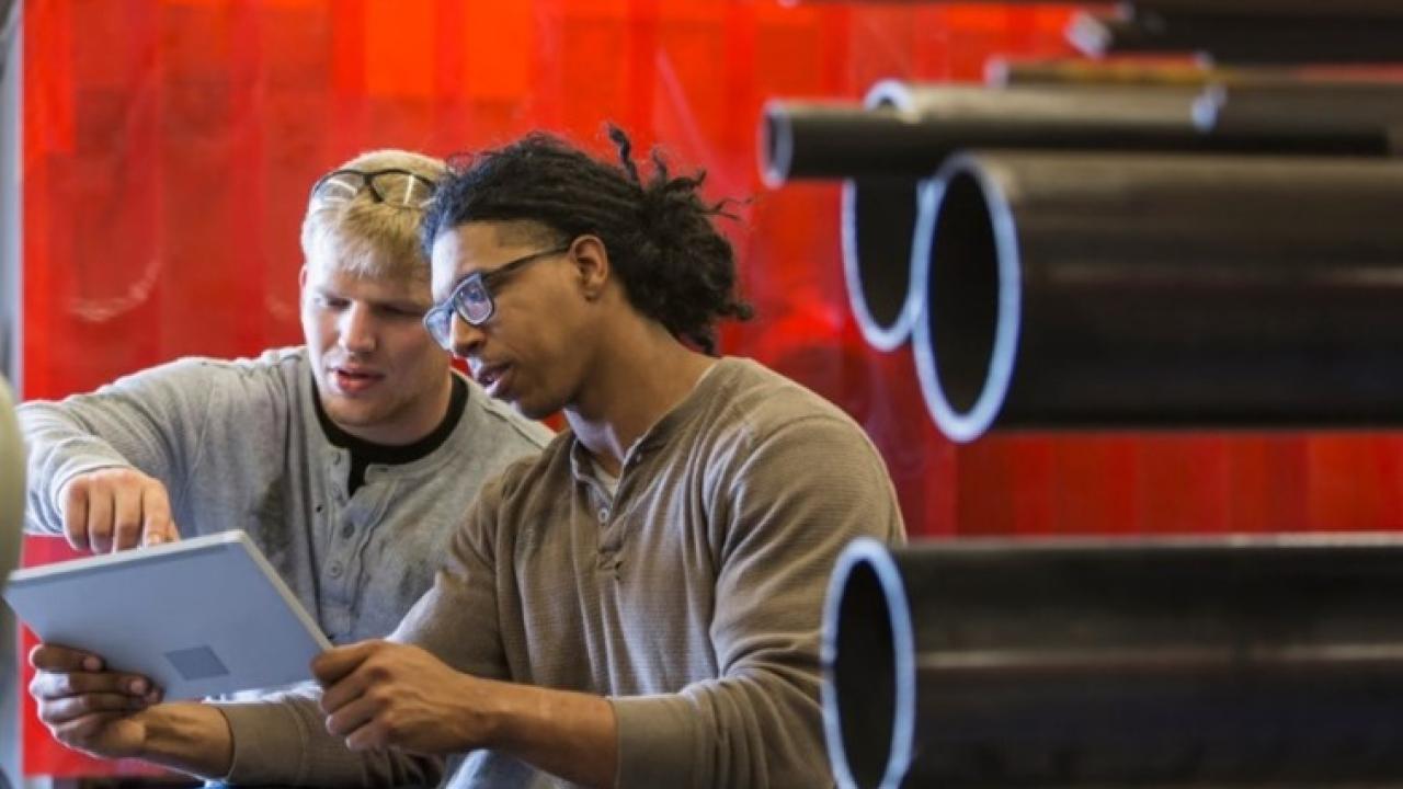 Two people looking at a laptop in a manufacturing facility.