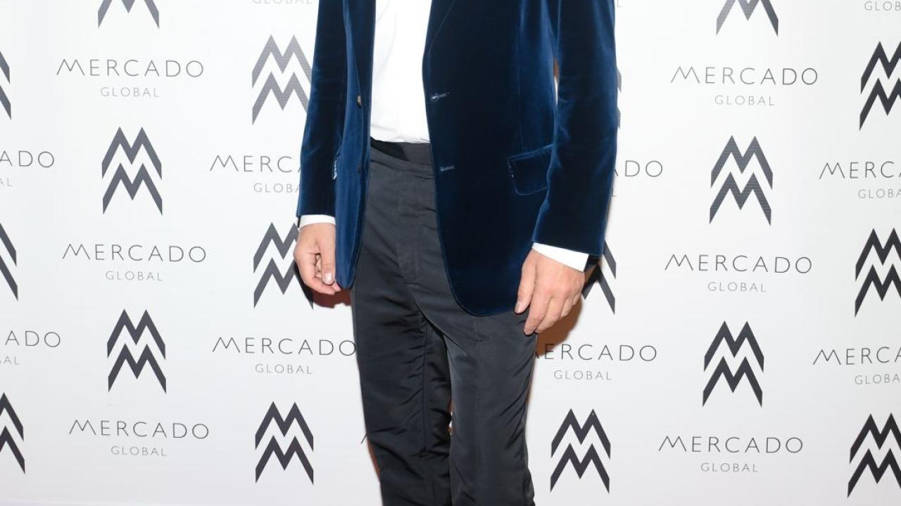 Edmundo Castillo on a red carpet, wall behind them has Mercado logos covering it.