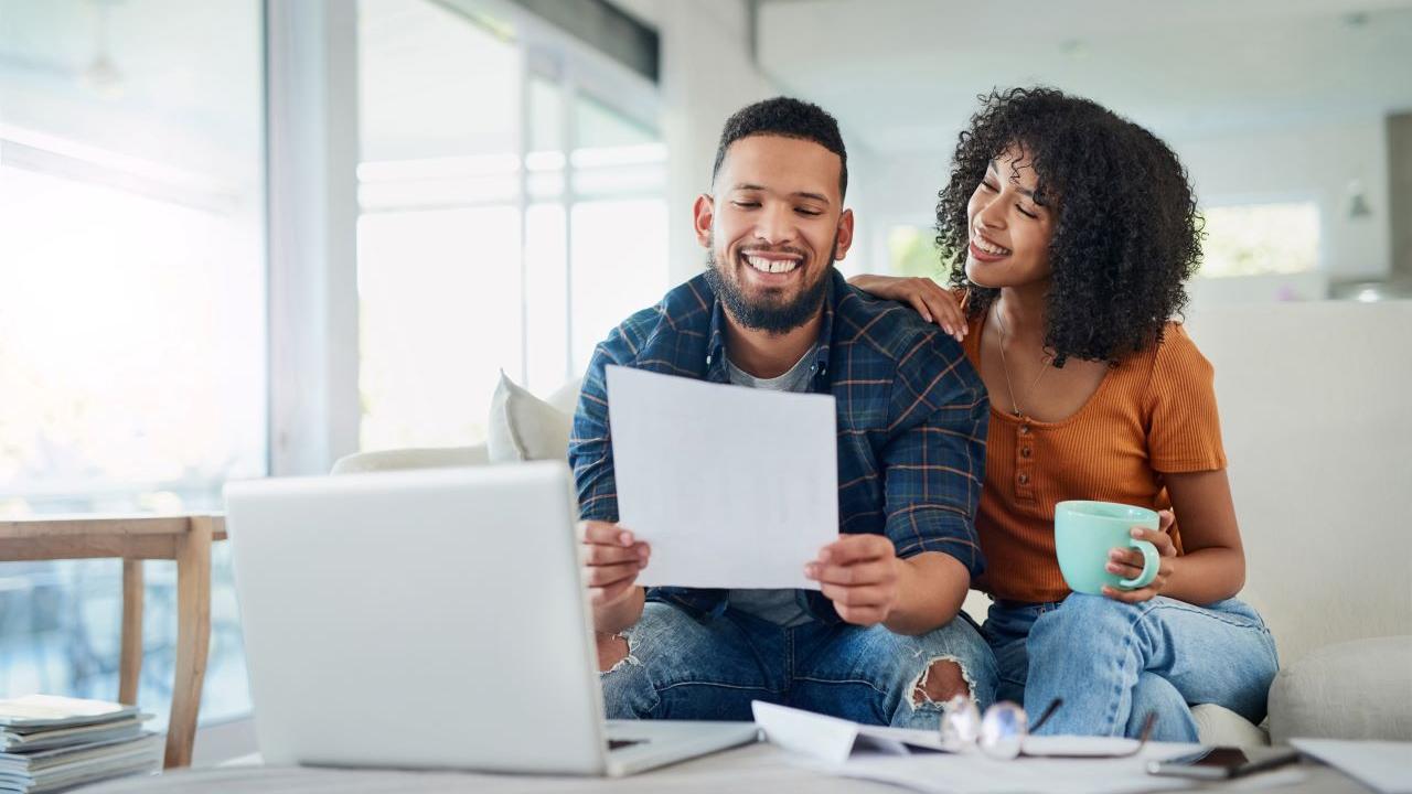 Smiling couple sitting on couch and looking at a piece of paper together