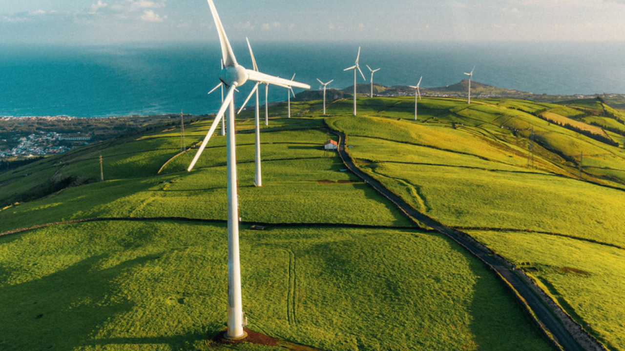 Windmills shown on top of a hill with green grass.