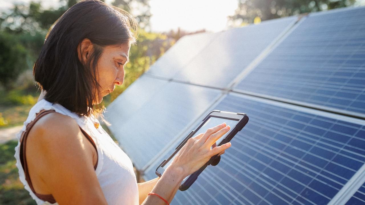 Woman holding a tablet and standing in front of a solar panel array.