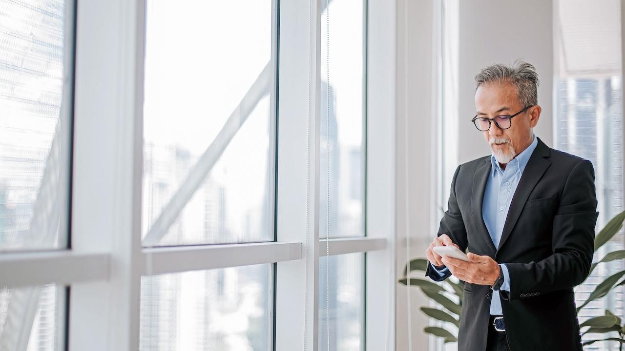 A person standing by a glass window looking at their phone.