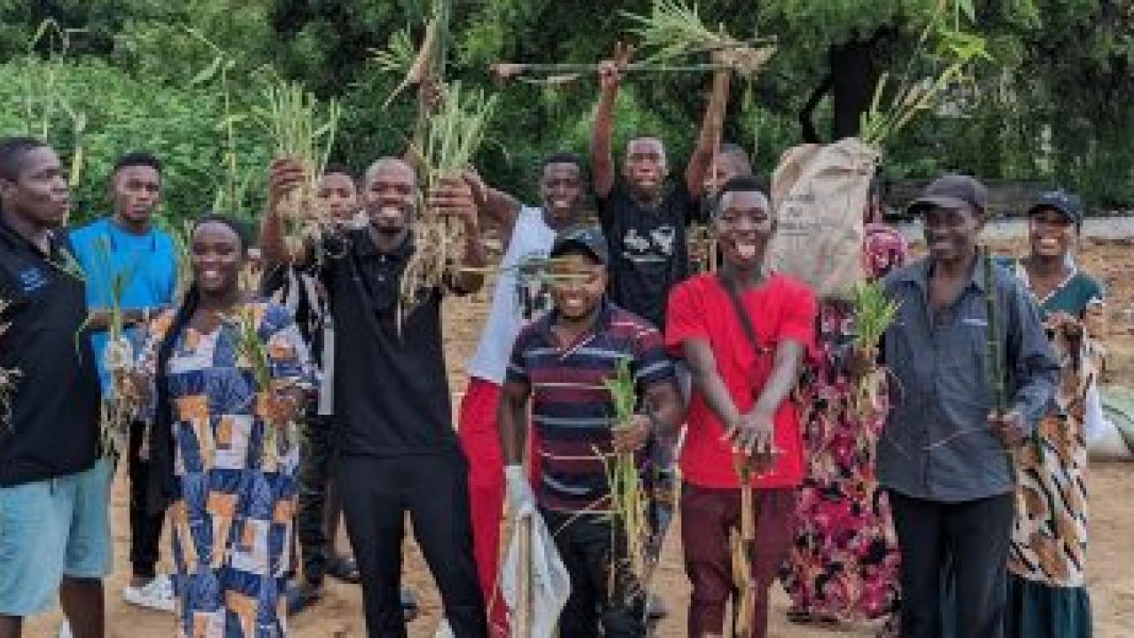 A group of smiling people posed outside, holding plants.